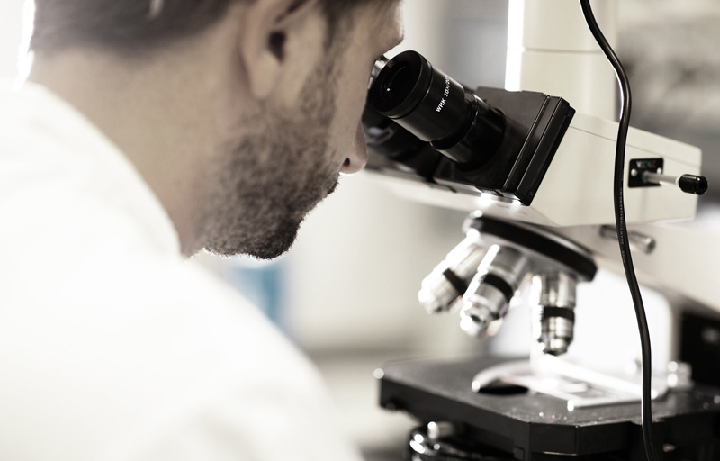 Tecnico in camice che analizza del prodotto al microscopio