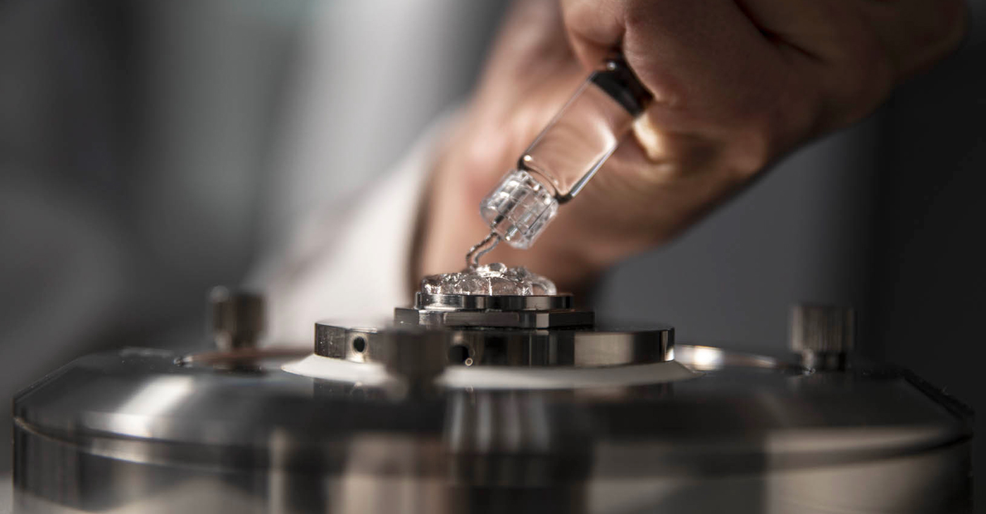 Tecnico posiziona con una siringa dell'acido ialuronico su uno strumento di analisi metallico.