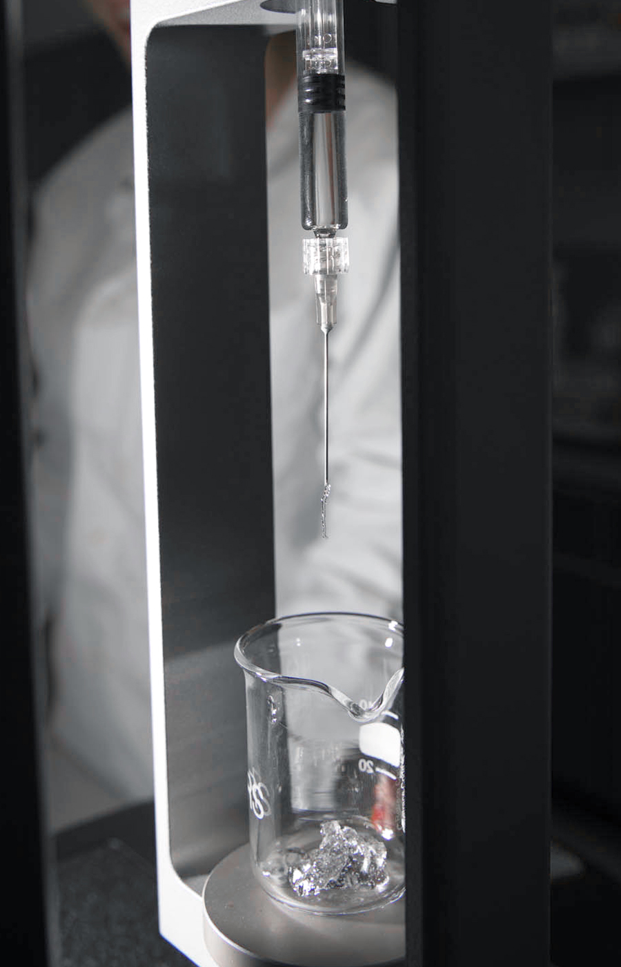 Dettaglio di un becher trasparente durante un test di viscosità con gocce di fluido in laboratorio.