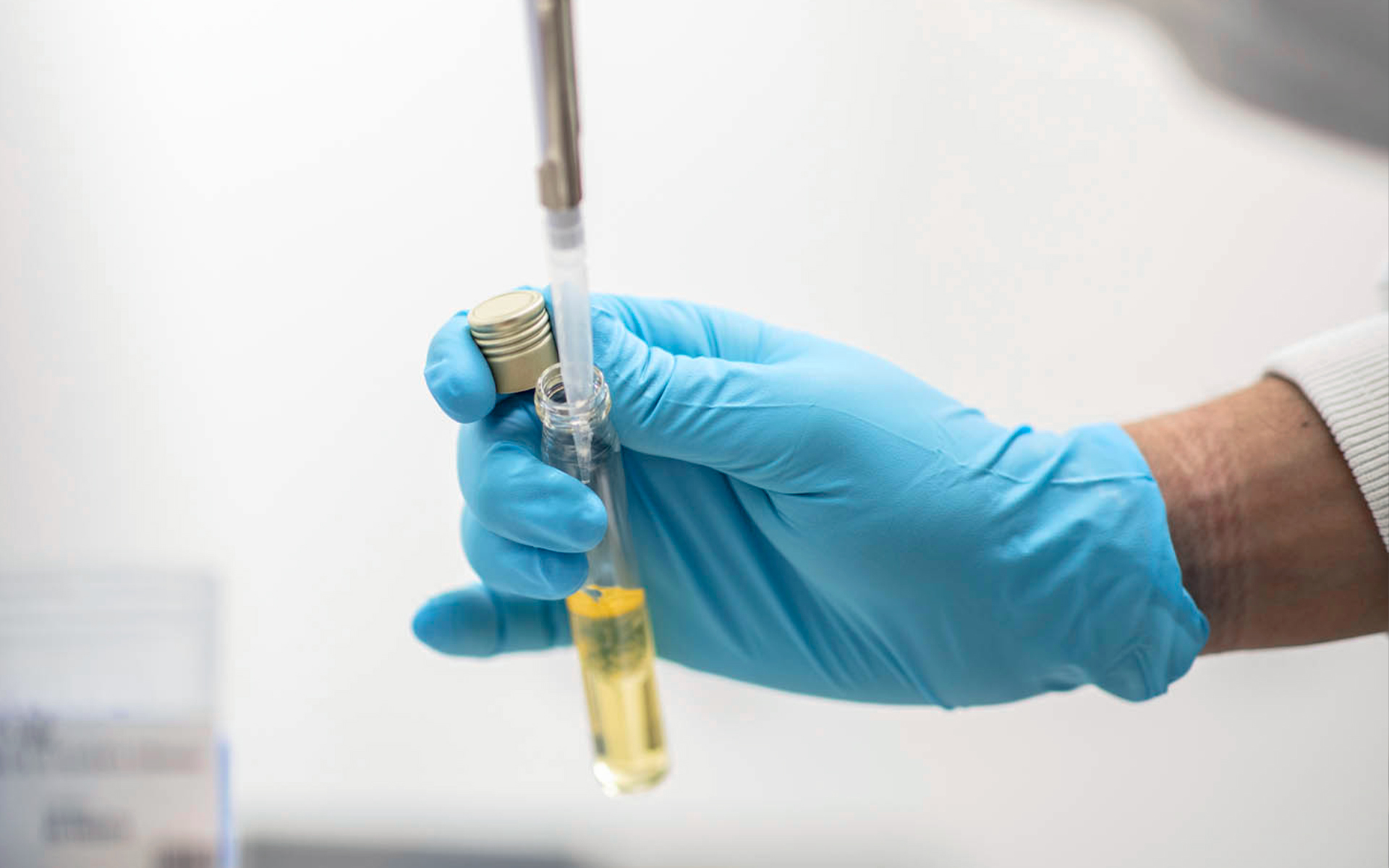 Mani con guanti azzurri che usano una pipetta per prelevare liquido da una fiala in laboratorio